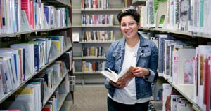 student in library holding a book and smiling